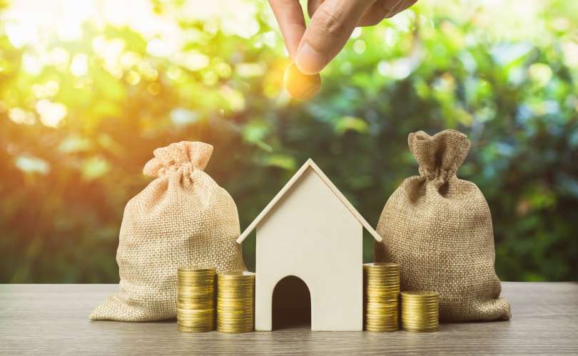 Saving money, home loan, mortgage, a property investment for future concept. A man hand putting money coin over small residence house and money bag with nature background. A sustainable investment.